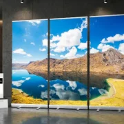 Eine weitläufige Andenlandschaft mit markanter Gebirgskette unter blauem Himmel. Im Vordergrund spiegelt ein glasklarer, tiefblauer See die Berge und Wolken fast vollkommen wider. Sanfte Uferzonen mit grün-gelblichen Farbtönen verleihen dem Motiv eine friedvolle Natürlichkeit.