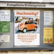 Modern gestalteter Gemeindeschaukasten mit dem christlichen DIN-A2-Hochformat-Poster „Hochmütig?“ von Edition Katzenstein. Das Poster zeigt einen klassischen Fiat 500 und ein inspirierendes Zitat von C. S. Lewis über Demut.