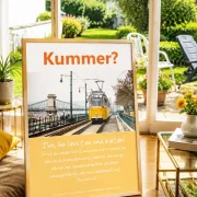 Hochwertiges Produktfoto des christlichen Posters „Kummer? – Ihn, ihn lass tun und walten!“ von Edition Katzenstein im Format DIN A2 in einem hellen Wohnzimmer mit Blick in einen gepflegten Garten.