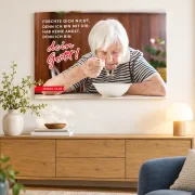 Leinwandbild Jahreslosung 2027 mit Seniorin und Bibelvers über einer Holzkommode, daneben eine Vase und eine Tischlampe.