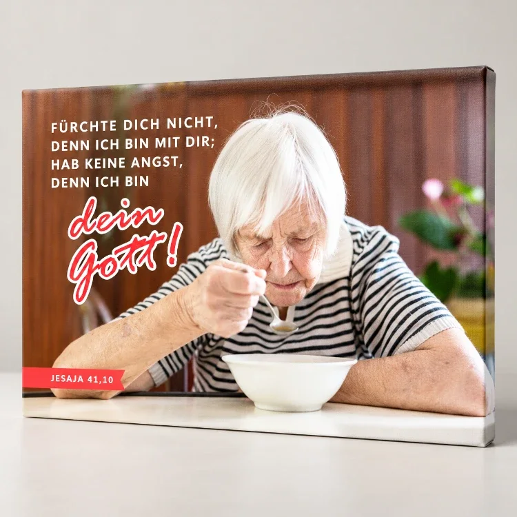 Leinwandbild Jahreslosung 2027 – Seniorin beim Essen auf Holzkeilrahmen Leinwandbild mit Seniorin beim Essen und Jesaja 41,10 in leicht seitlicher Studioansicht mit sichtbarer Leinwandstruktur.