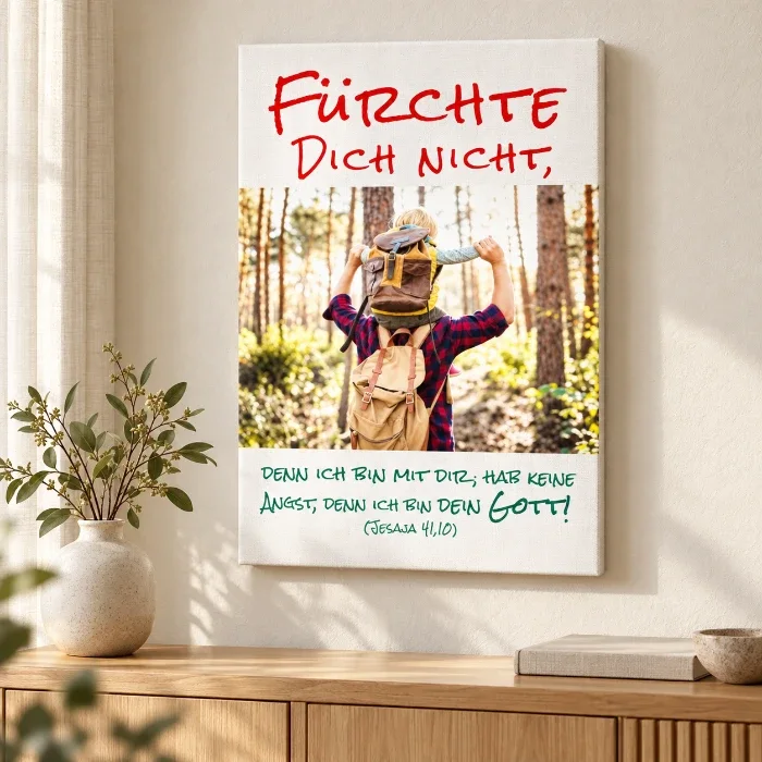 Jahreslosung 2027 auf Leinwand – Geborgenheit im Zuhause Leinwandbild zur Jahreslosung 2027 mit Vater-Sohn-Motiv über einer Holzkommode neben einer Vase im hellen Wohnzimmer.
