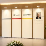Vier aufsteckbare LED-Leuchten beleuchten ein vierteiliges Roll-Up-Gedenkset in einer modernen Trauerhalle