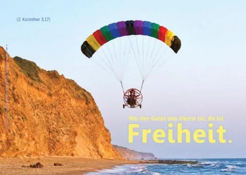 Ein Motorgleitschirm schwebt hoch über einer imposanten Steilküste im Sonnenlicht; christliches A2-Poster zu Pfingsten mit Bibelvers aus 2. Korinther 3,17.