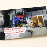 Freigestelltes DIN-A1-Poster zur Jahreslosung 2027 mit Feuerwehrmann und älterem Ehepaar - Edition Katzenstein