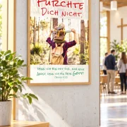 Gerahmtes DIN-A2-Poster zur Jahreslosung 2027 mit Vater und Sohn im hellen Foyer eines Gemeindezentrums