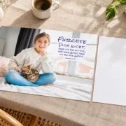 DIN-A3-Poster zur Jahreslosung 2027 mit Mädchen und Katze neben einem A4-Blatt auf einem Leinentisch