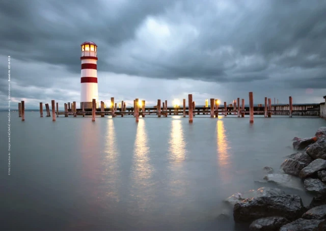Leuchtturm vor dunklen Regenwolken, aufgenommen aus der Distanz.
