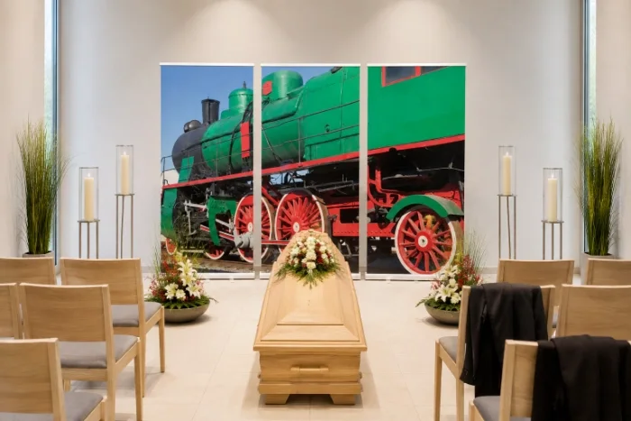 Dreiteiliges Roll-Up Display mit historischer grüner Dampflok als Hintergrund hinter einem hellen Eschenholzsarg in einer modernen deutschen Trauerhalle.